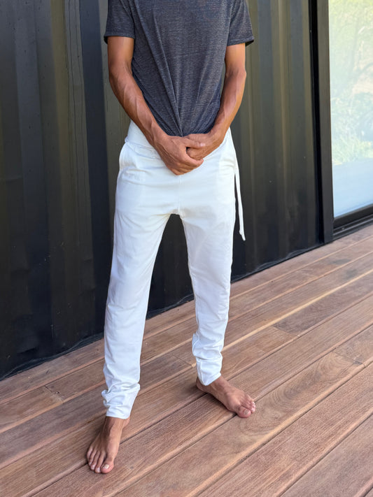 male model standing in white skinny wander pants by glorka in front of the black wall on wooden floor