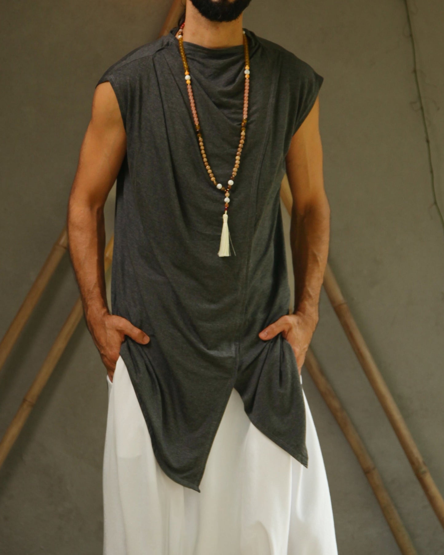 Man wearing glorka sleeveless top and white pants standing against a neutral background with decorative elements.