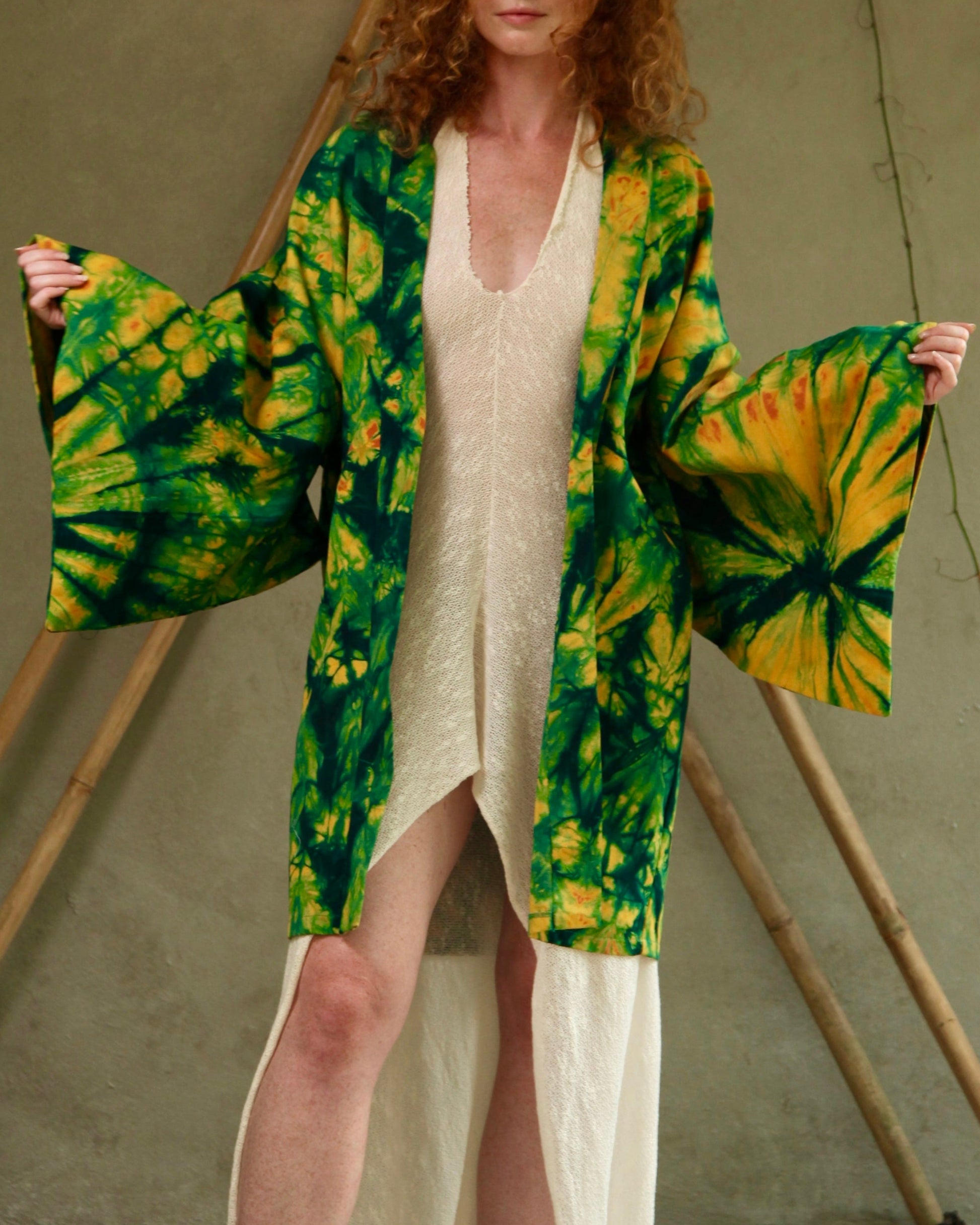 Woman wearing a green and yellow tie-dye kimono over a white dress, standing against a neutral background.