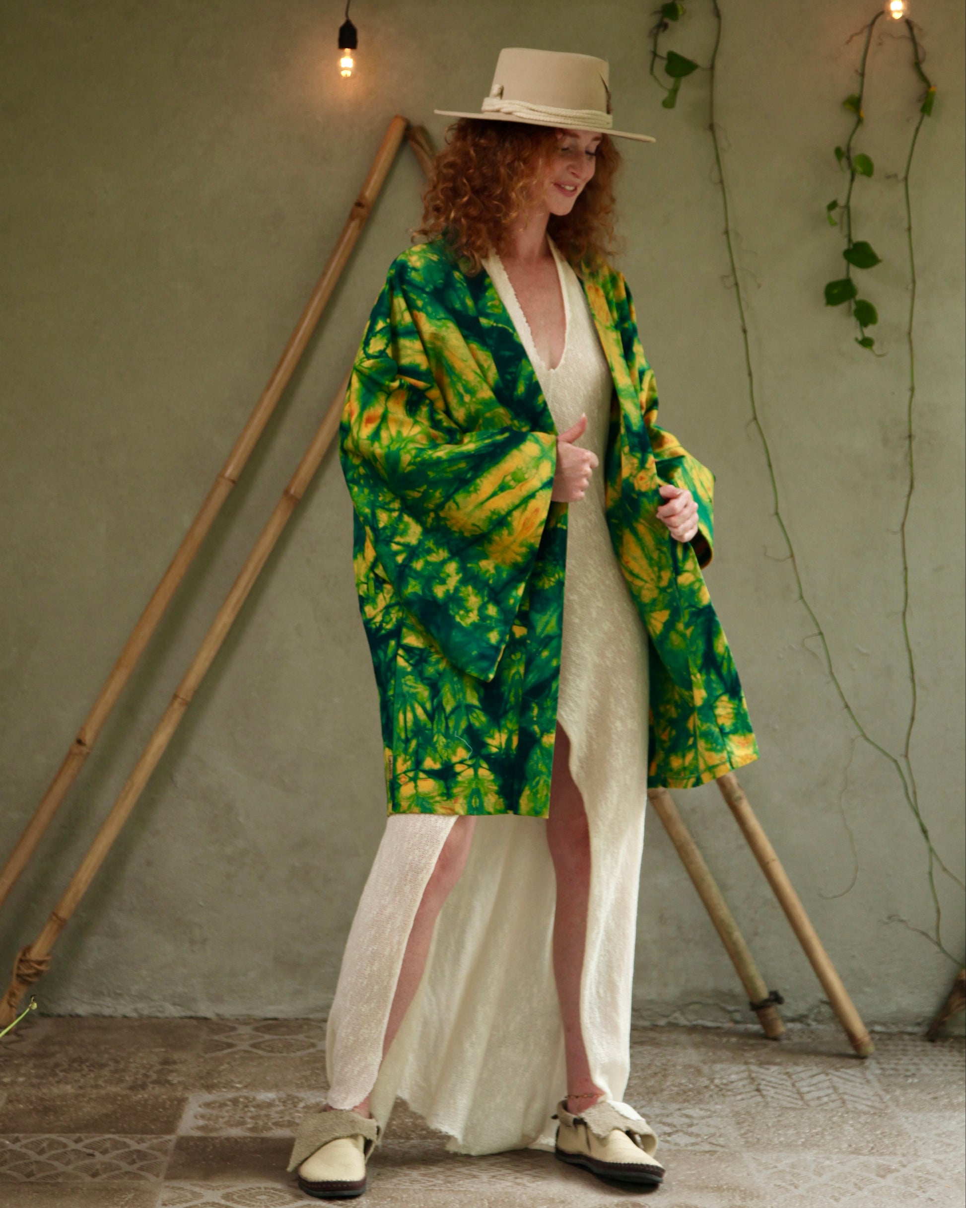 Woman wearing a green and yellow patterned kimono over a white dress in a rustic setting.