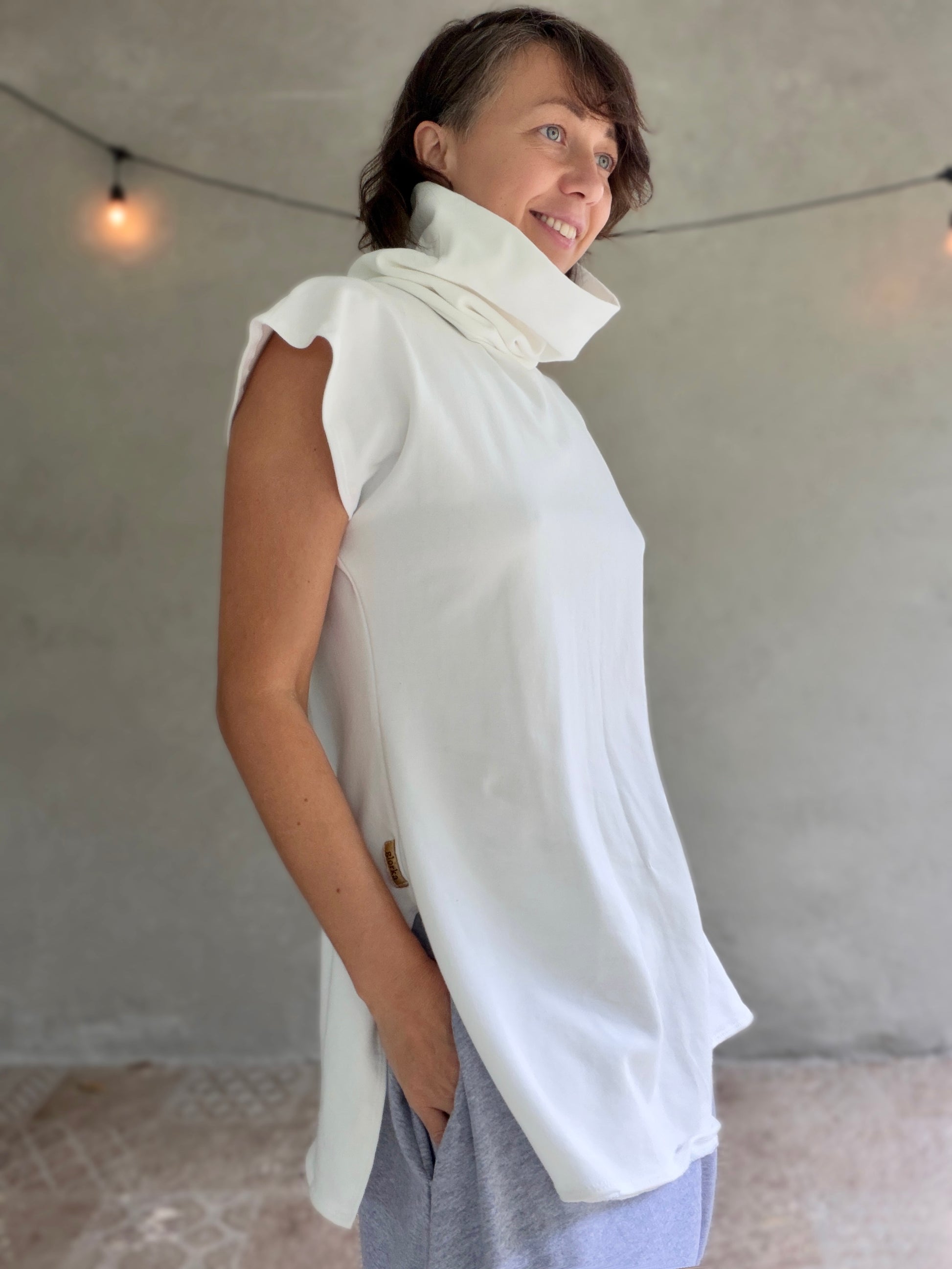 Woman wearing a white sleeveless top with a high collar against a plain background