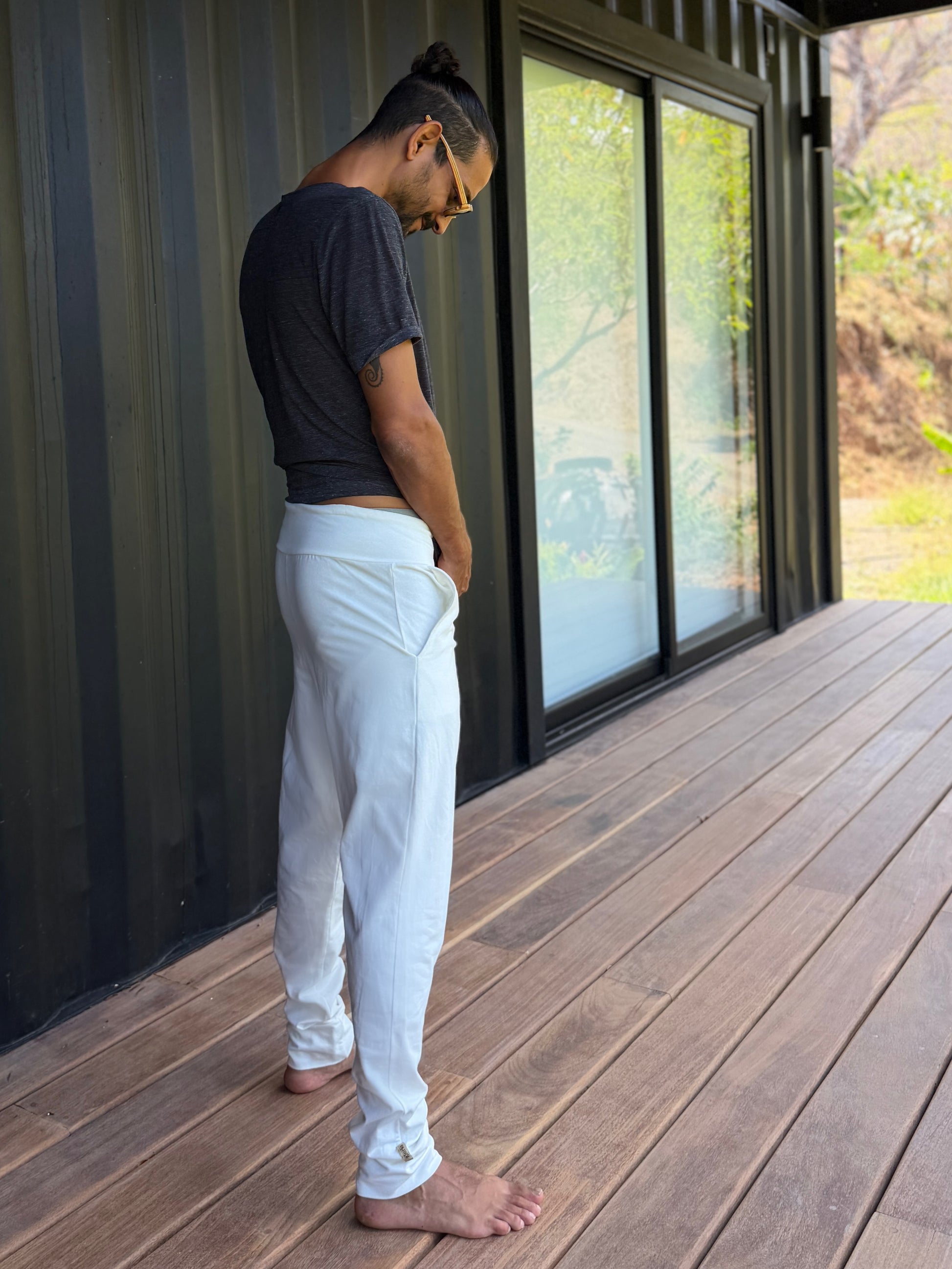 male model standing in white skinny wander pants by glorka in front of the black wall on wooden floor