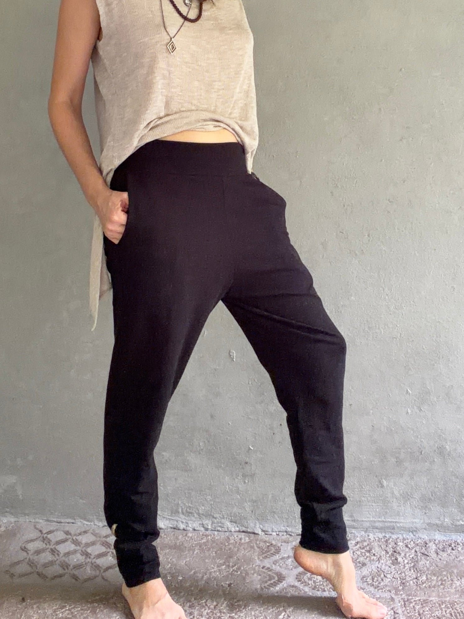 Person wearing black pants and a beige top against a gray wall.