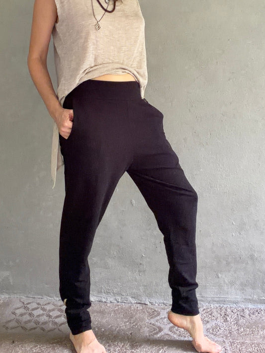 Person wearing black pants and a beige top against a gray wall.