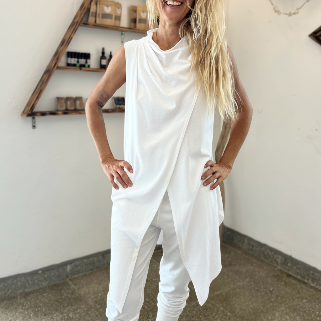 Person wearing a white sleeveless top and pants in a room with shelves in the background.