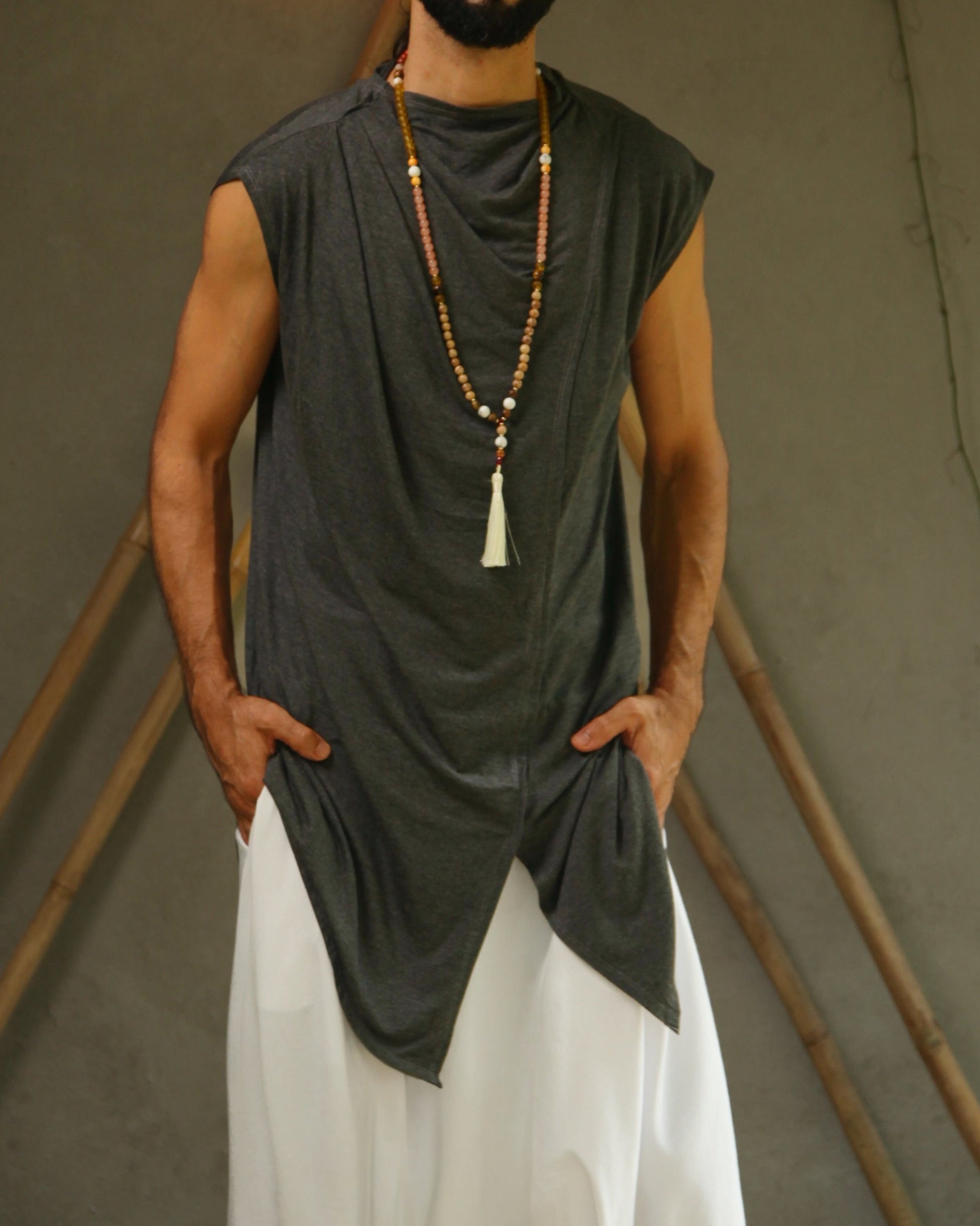 Man wearing glorka sleeveless top and white pants standing against a neutral background with decorative elements.