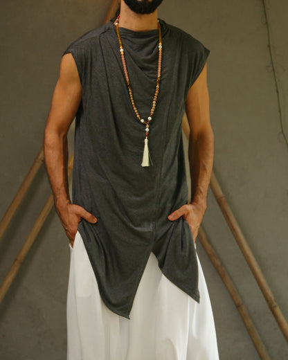 Man wearing glorka sleeveless top and white pants standing against a neutral background with decorative elements.