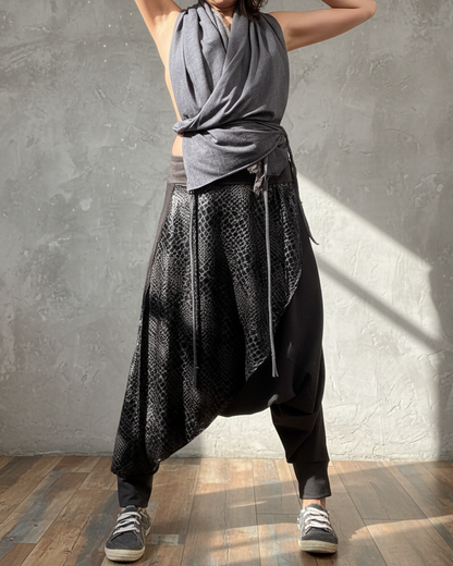 Person wearing a gray top and black patterned glorka pants against a concrete wall.