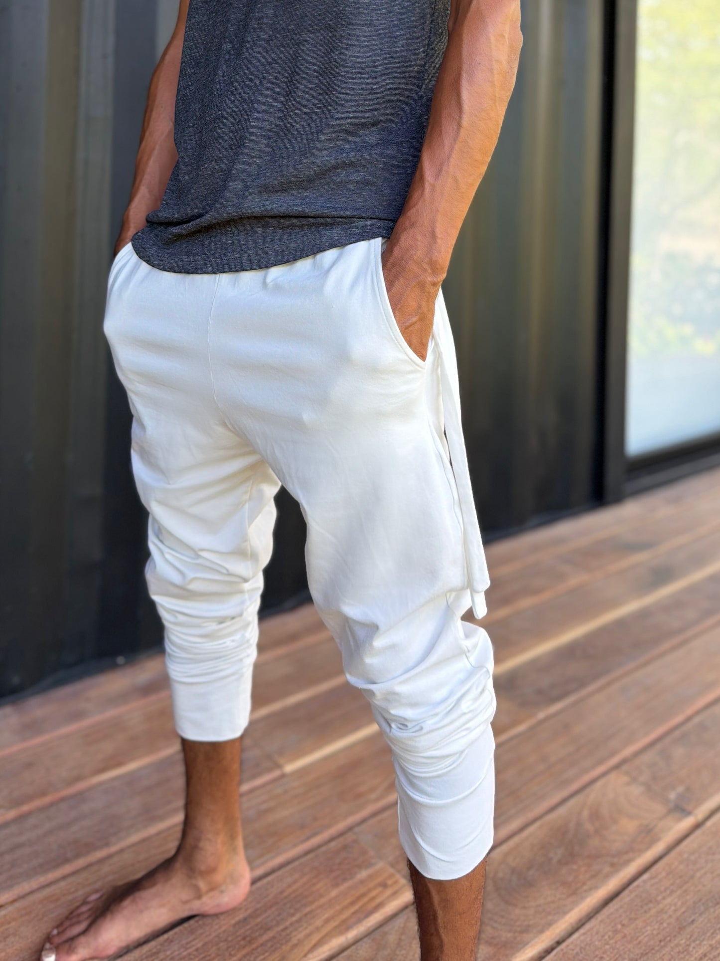 male model standing in white skinny wander pants by glorka in front of the black wall on wooden floor