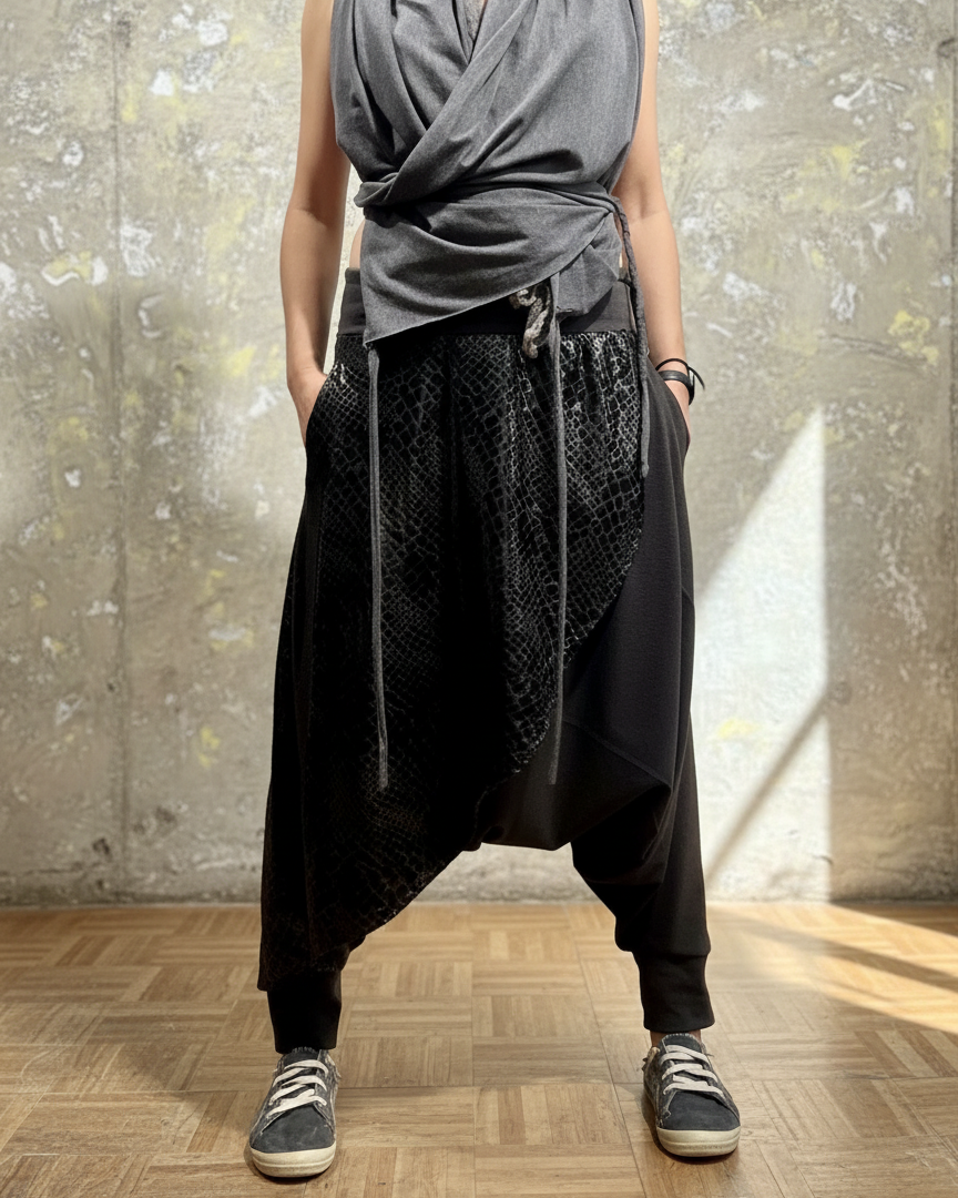 Person wearing a sleeveless gray top and black harem pants against a textured wall.
