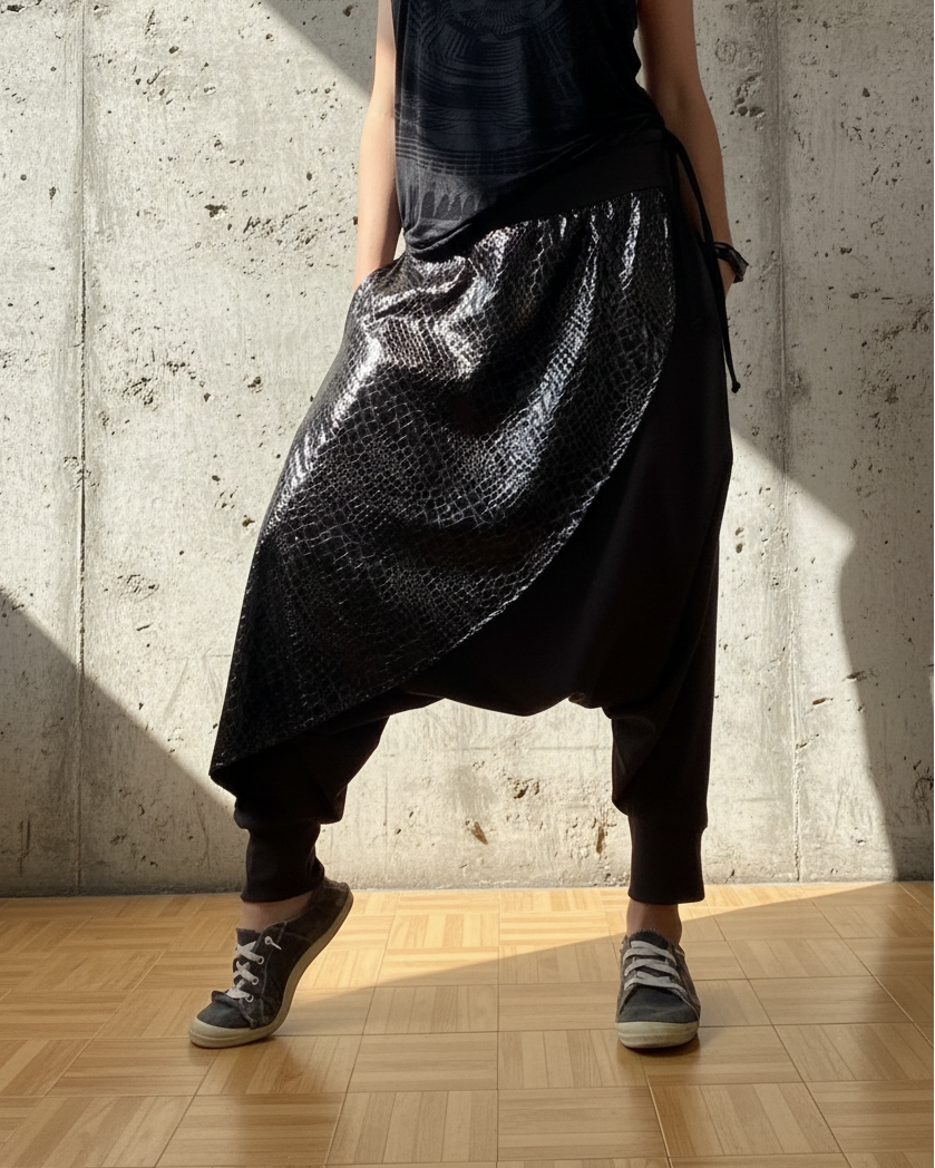 Person wearing a black sleeveless top and shiny black pants against a concrete wall.