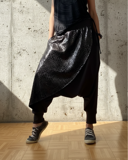 Person wearing a black sleeveless top and shiny black pants against a concrete wall.