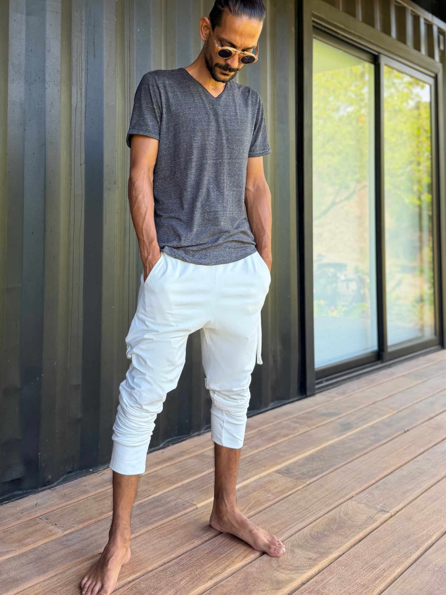male model standing in white skinny wander pants by glorka in front of the black wall on wooden floor