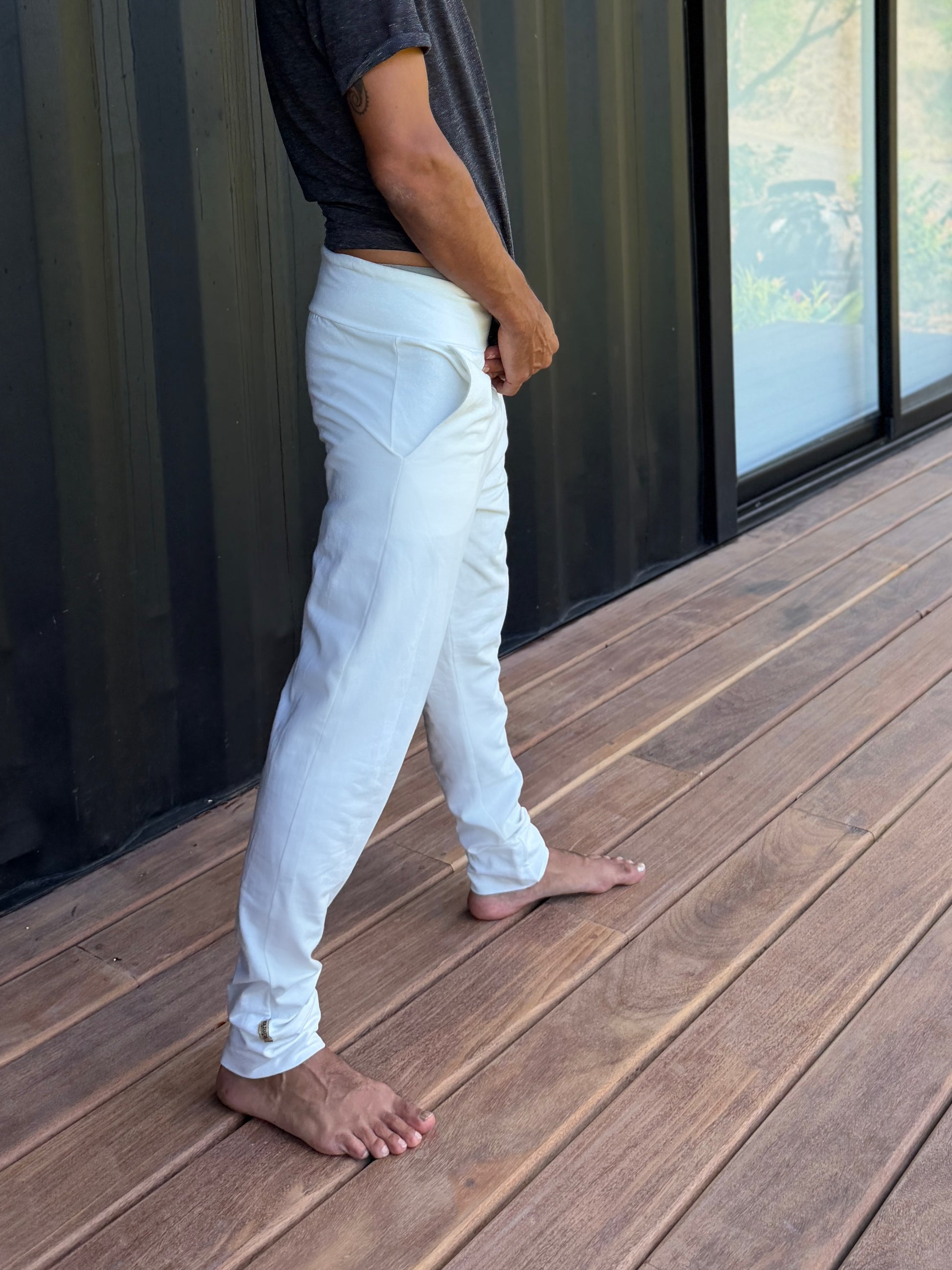 male model standing in white skinny wander pants by glorka in front of the black wall on wooden floor