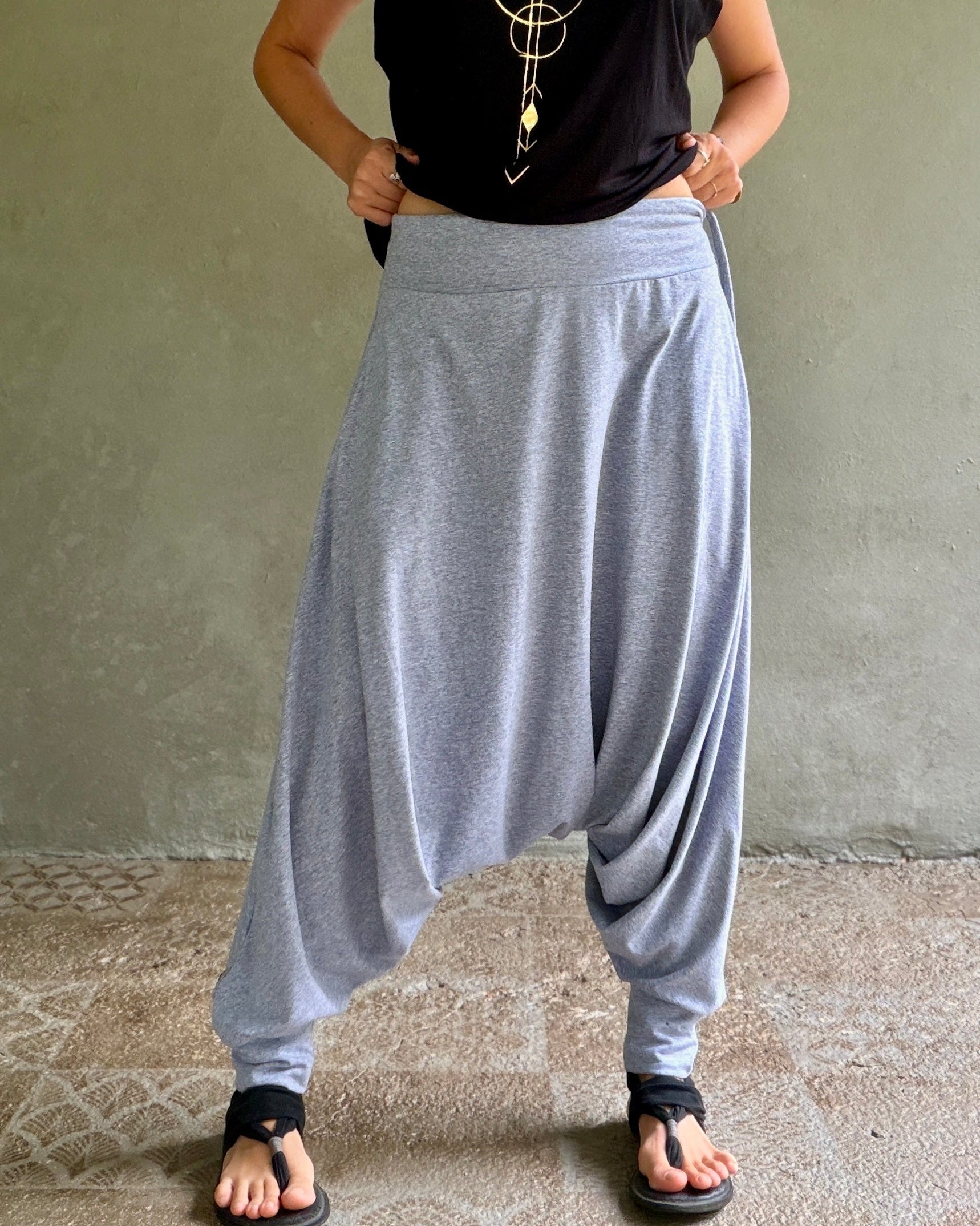 Person wearing gray harem pants and a black top against a neutral background