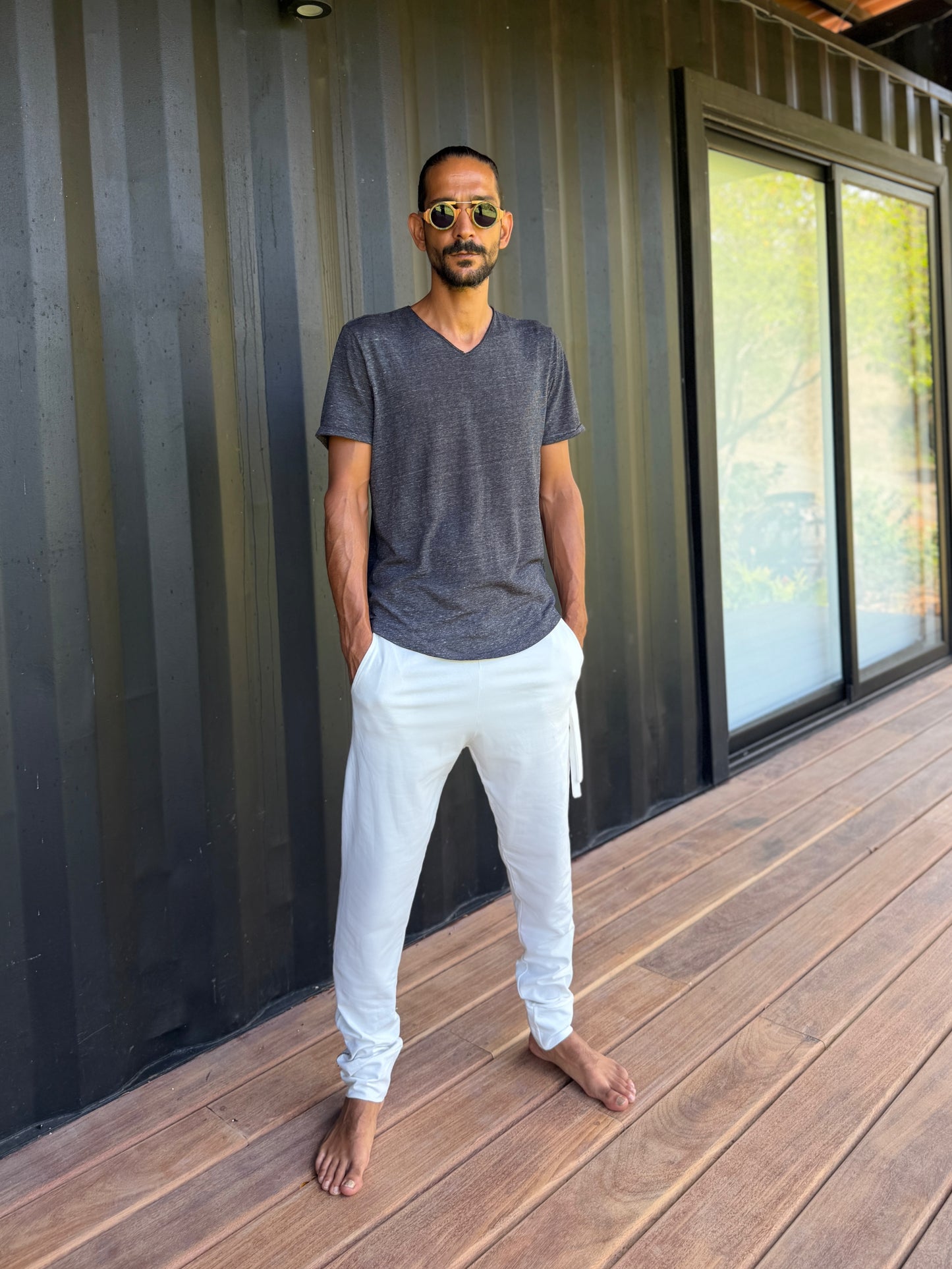 male model standing in white skinny wander pants by glorka in front of the black wall on wooden floor