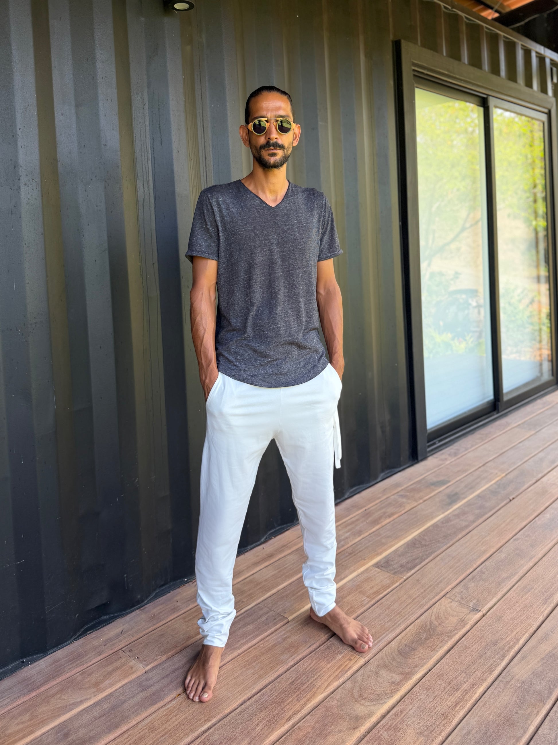 male model standing in white skinny wander pants by glorka in front of the black wall on wooden floor