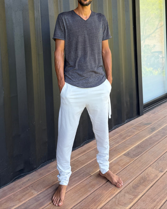 male model standing in white skinny wander pants by glorka in front of the black wall on wooden floor