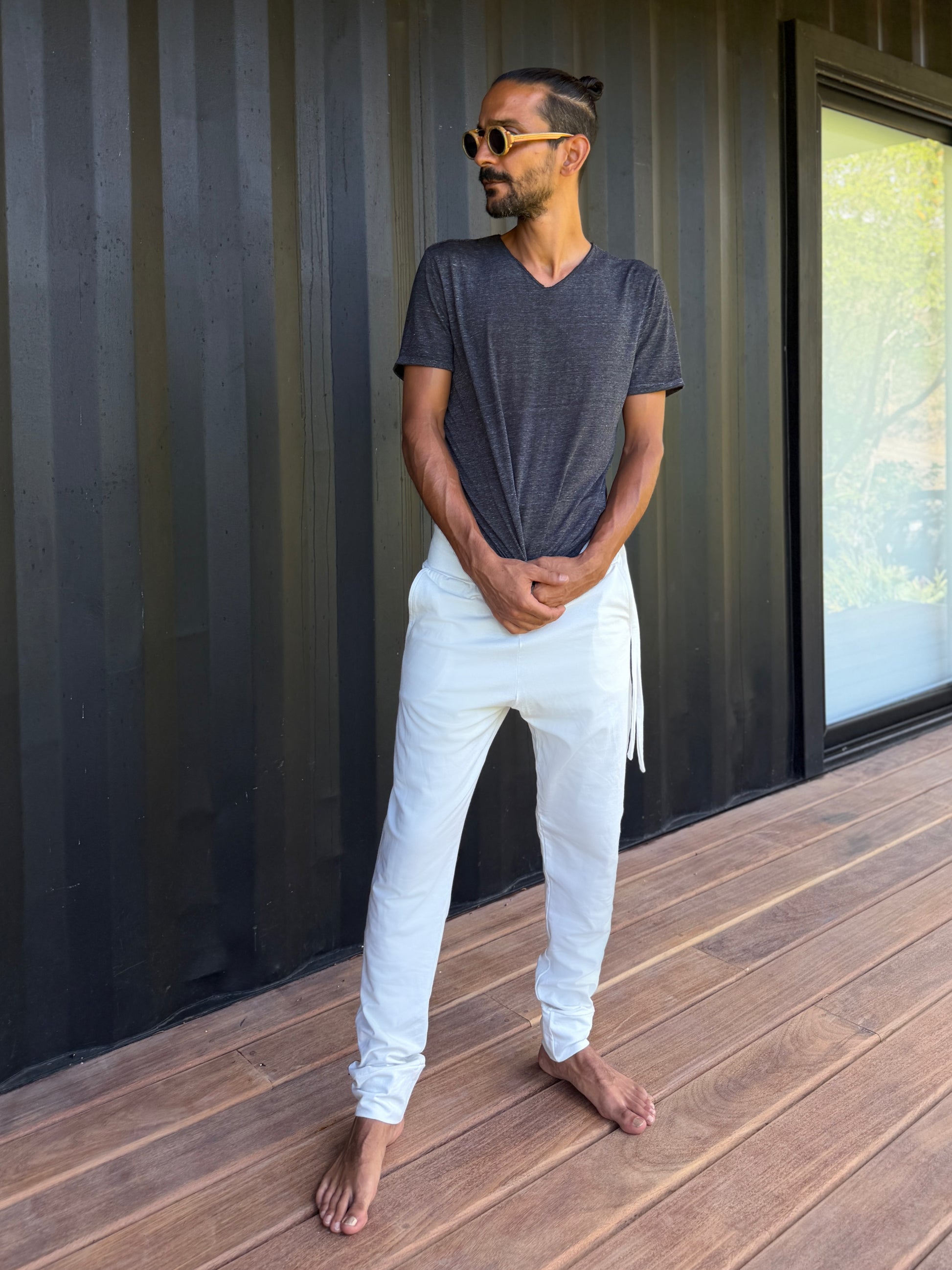 male model standing in white skinny wander pants by glorka in front of the black wall on wooden floor