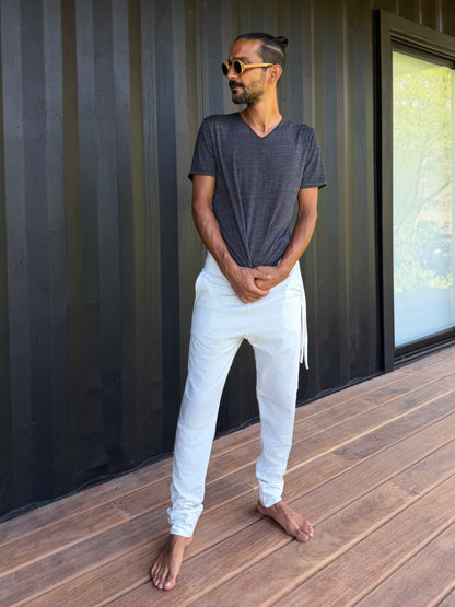 male model standing in white skinny wander pants by glorka in front of the black wall on wooden floor