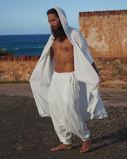 Man in white clothing standing by a coastal wall with ocean view