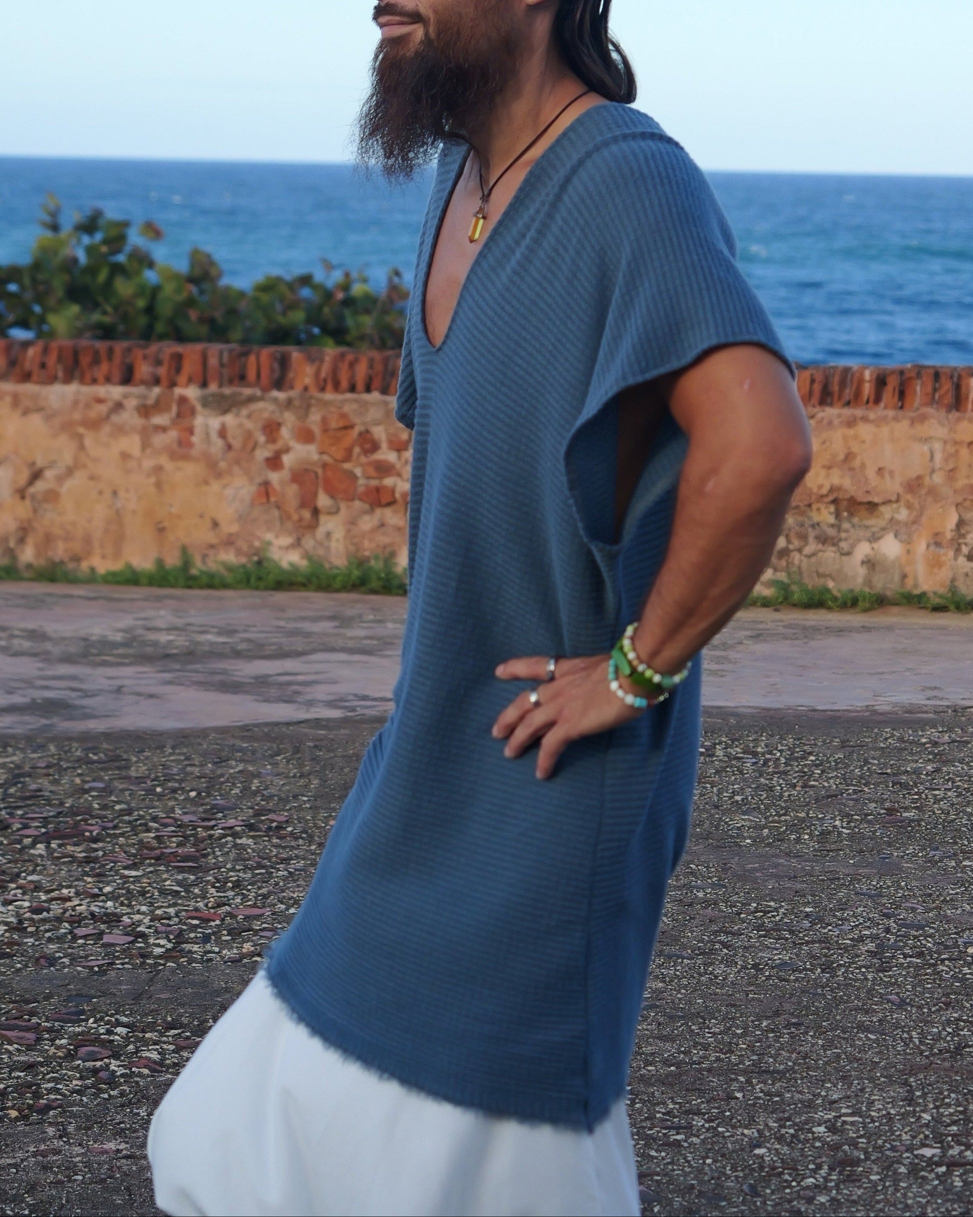 Man wearing a blue and white outfit standing on a road with ocean and wall in the background