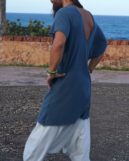 Man in blue shirt and white pants standing on a road with ocean and wall in the background