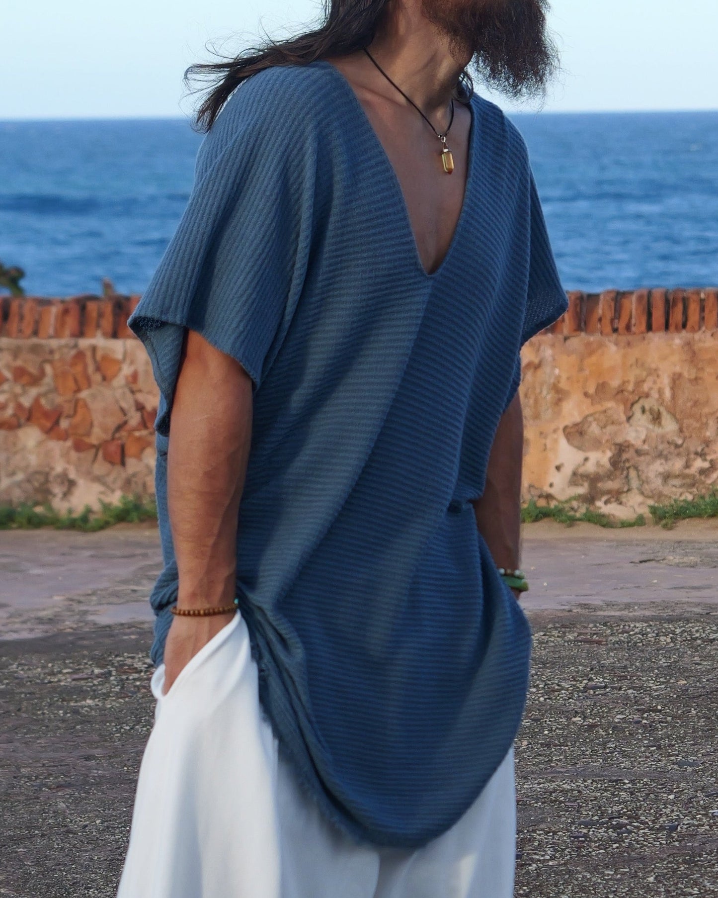 Man in blue shirt and white pants standing on a road with ocean and sky in the background
