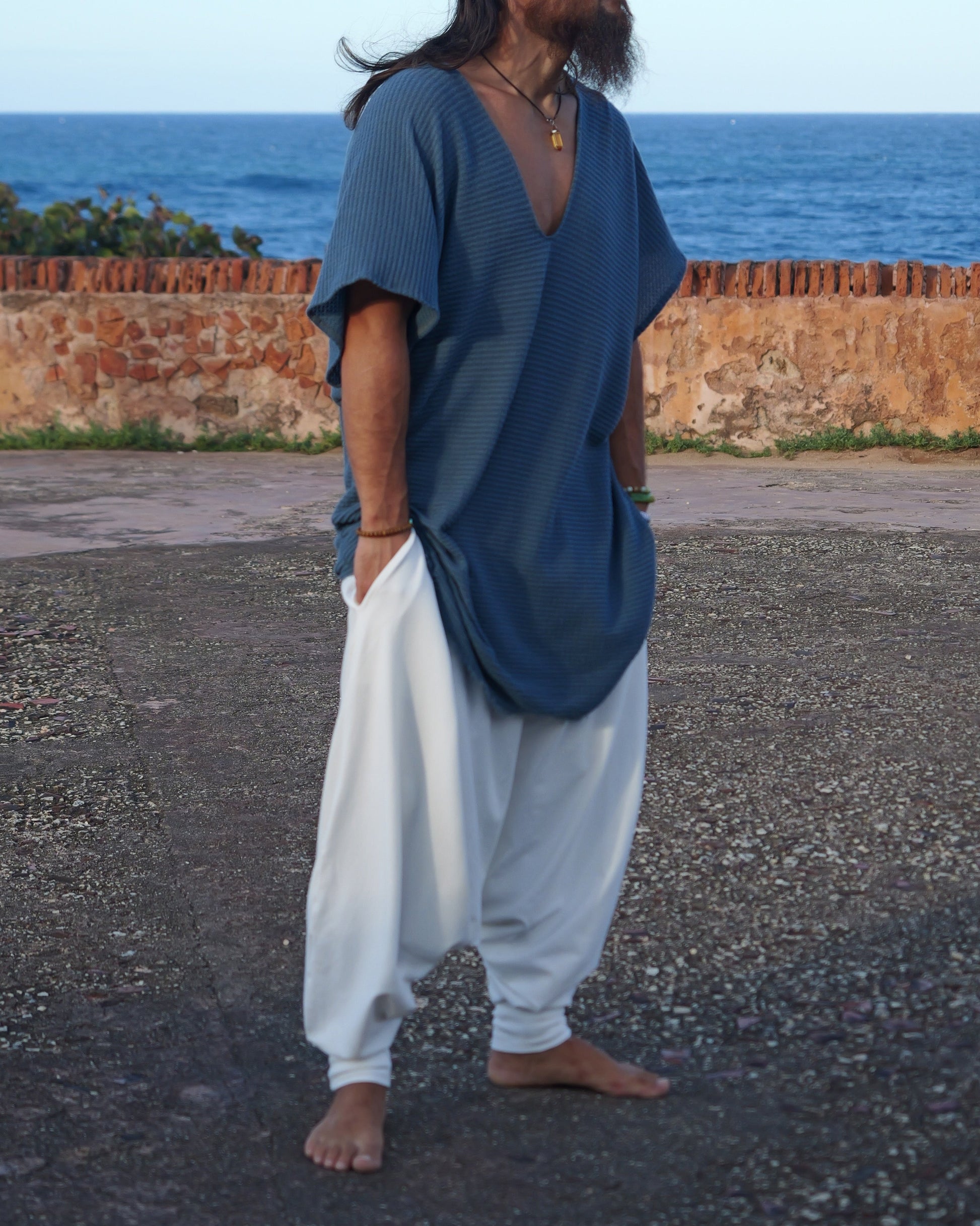 Man in blue shirt and white pants standing by a coastal wall with ocean view