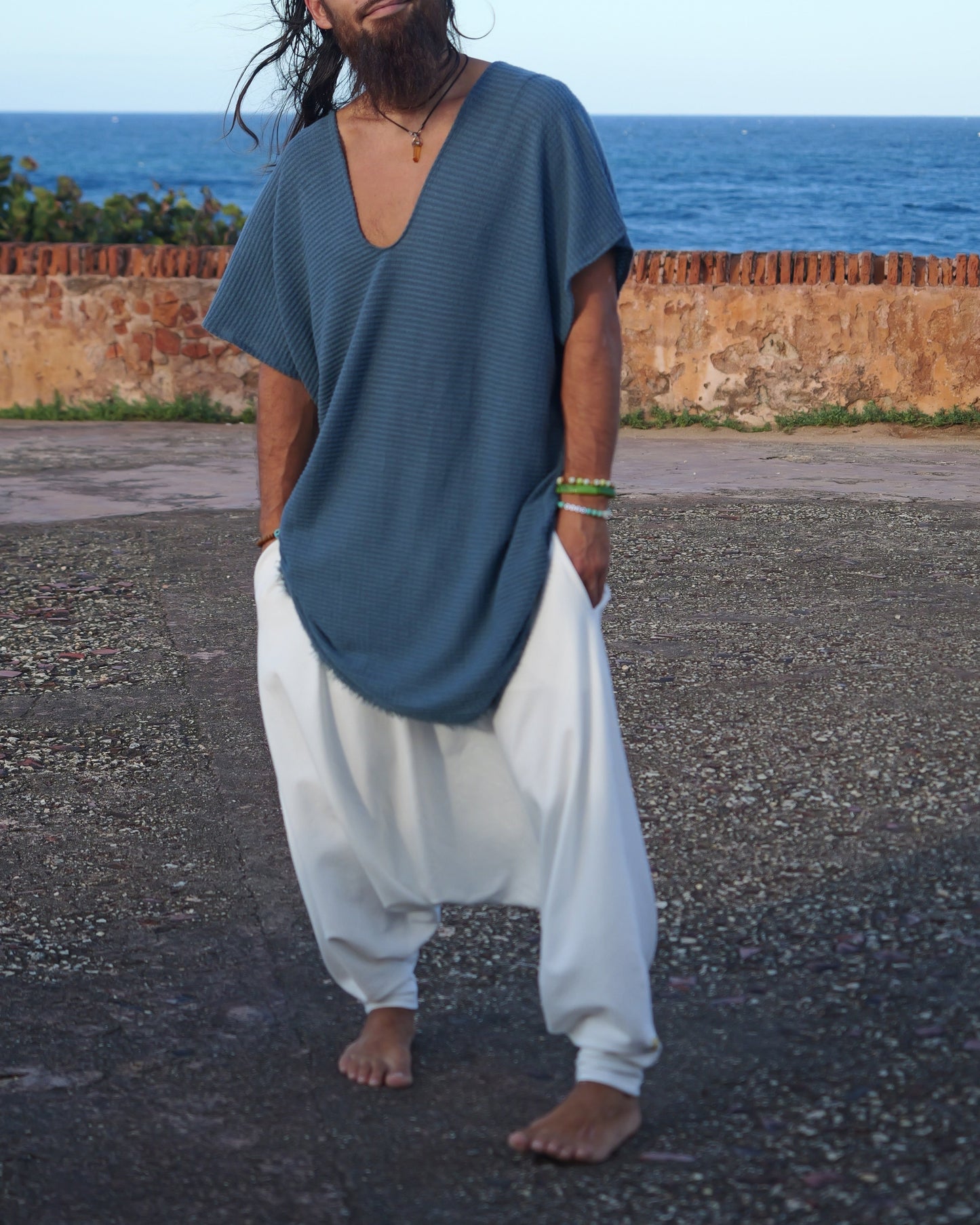 Man wearing a blue shirt and white pants standing in front of an ocean view.