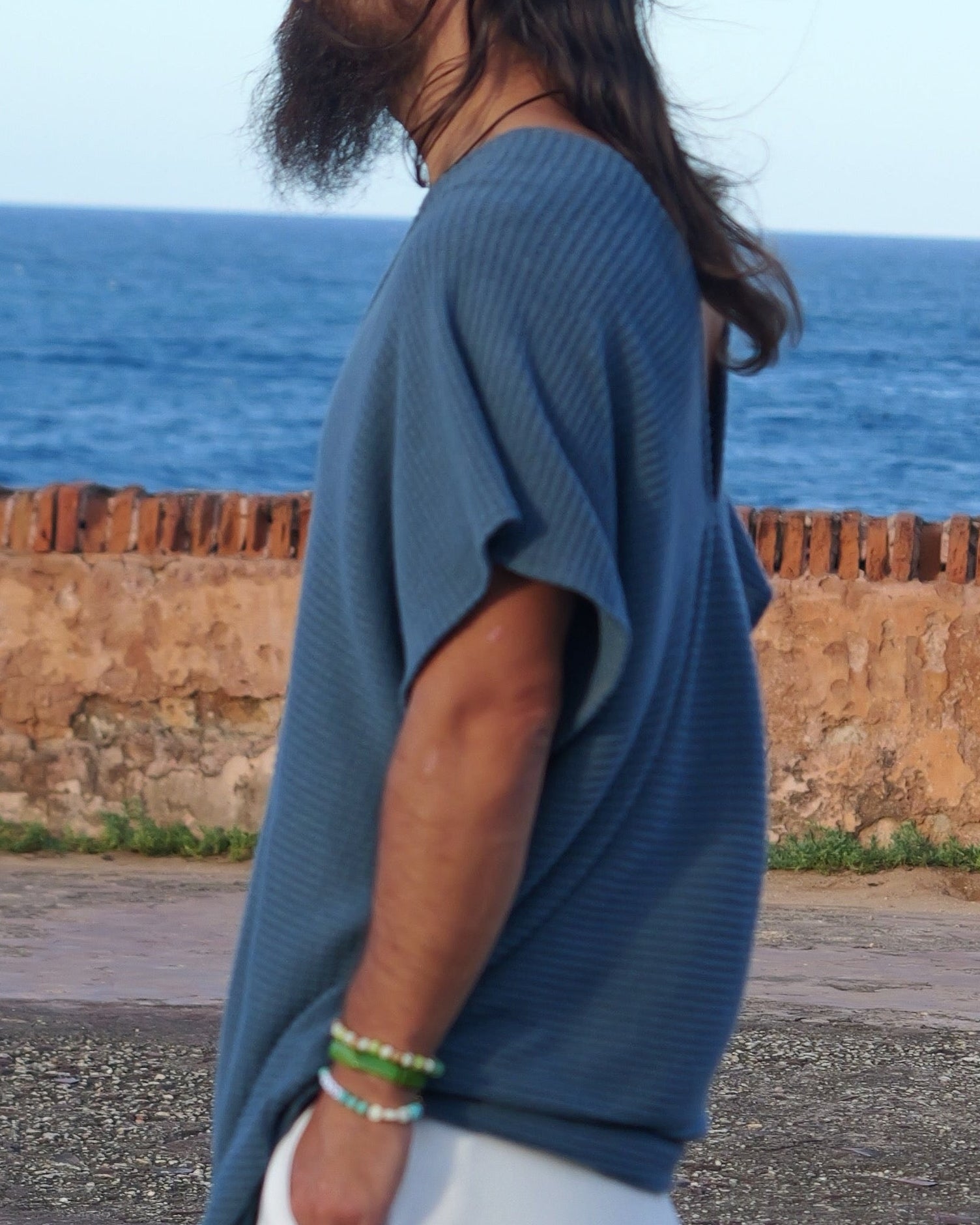 Man standing by the ocean with a brick wall and blue sky in the background