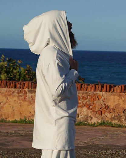 Person in a white outfit standing on a textured surface with a clear blue sky.