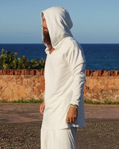 Person in a white outfit standing on a road with a blue sky and stone wall in the background