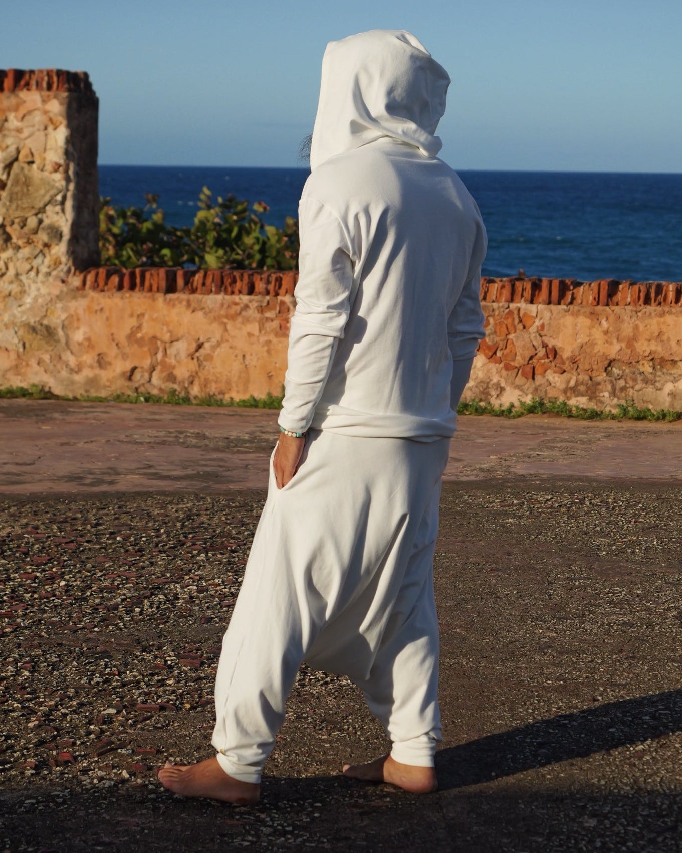 Person in a white outfit standing on a gravel path with a clear blue sky.