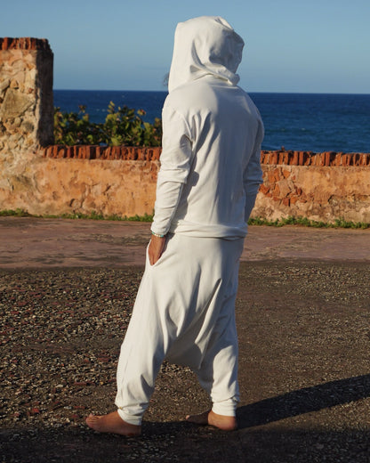Person in a white outfit standing on a gravel path with a clear blue sky.