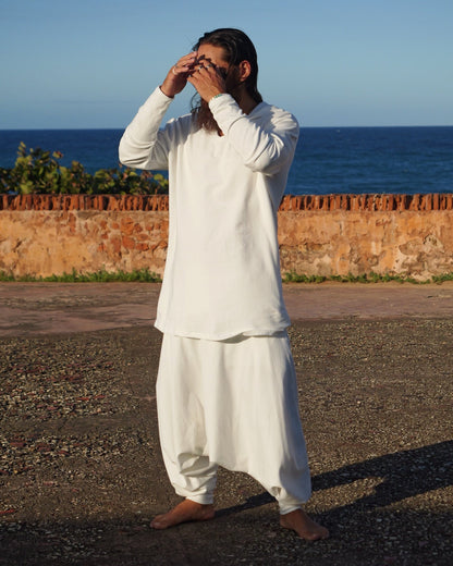 Person in a white outfit standing on a road with a blue wall and brick wall in the background