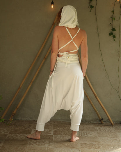 Person wearing a white outfit with criss-cross straps in front of a beige wall with string lights.