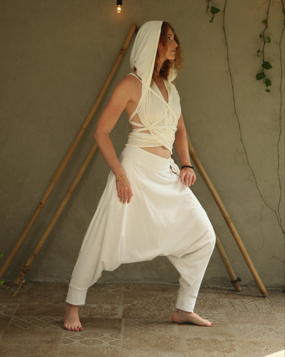 Woman in a white outfit standing in a room with a beige wall and wooden sticks.