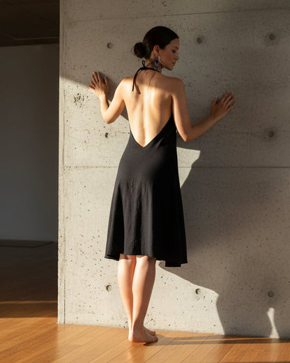 Woman in a black dress standing against a concrete wall with sunlight casting shadows.