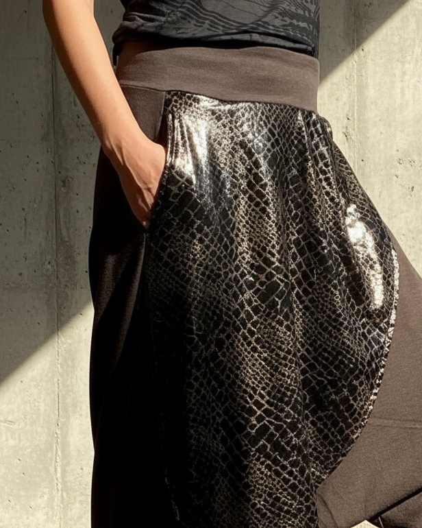 Person wearing a unique outfit with a patterned top and snake skin harem glorka pants against a concrete wall.