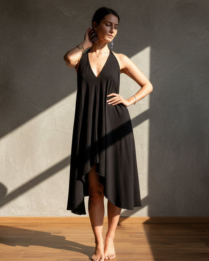 Woman wearing a black dress standing against a gray wall with a wooden floor.