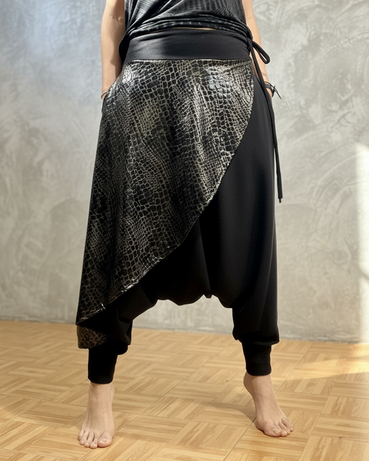 Person wearing a black and patterned glorka harem pants on a wooden floor with a gray wall background