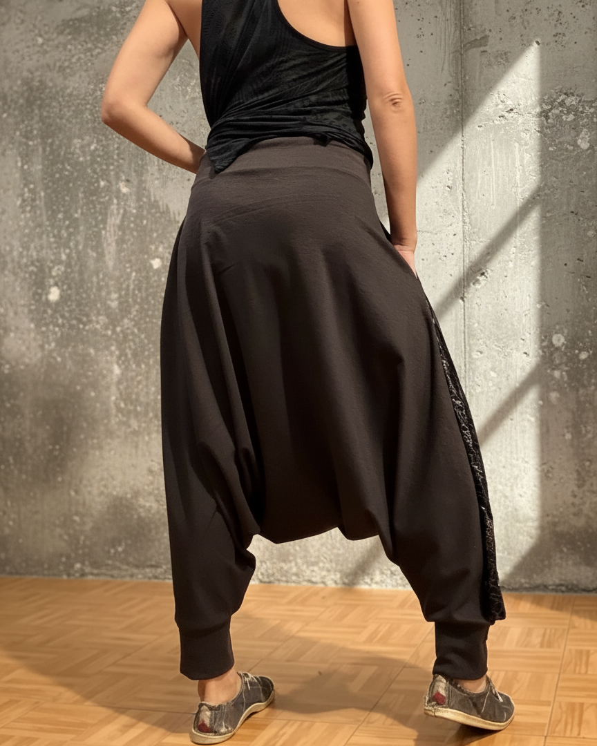 Person wearing black loose-fitting glorka pants and a black top against a concrete wall.