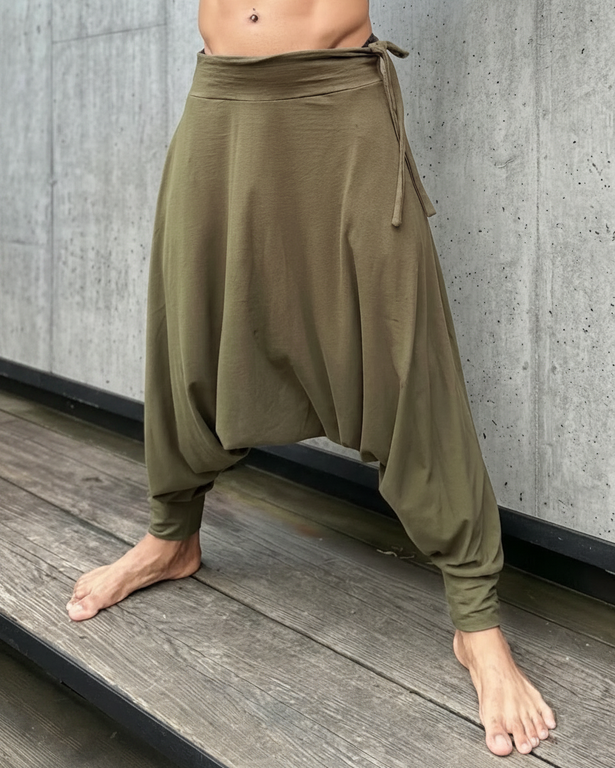 Person wearing olive green baggy pants standing on a wooden floor with a gray concrete wall in the background.