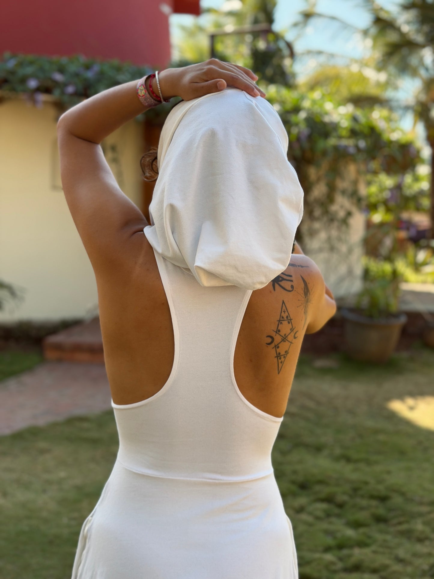 Person in a white hooded glorka Aura jumper with a tattoo on their arm, standing outdoors with greenery in the background.