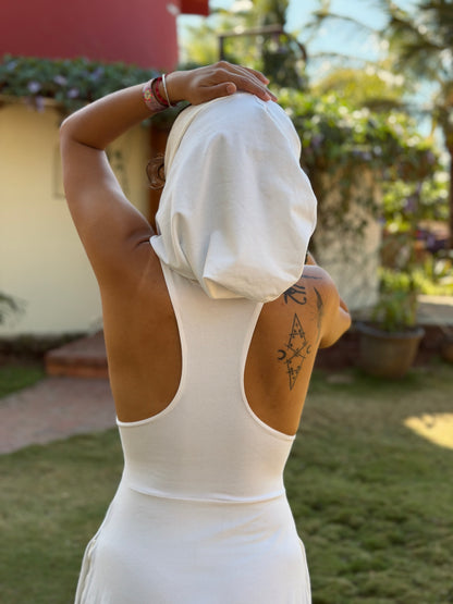 Person in a white hooded glorka Aura jumper with a tattoo on their arm, standing outdoors with greenery in the background.