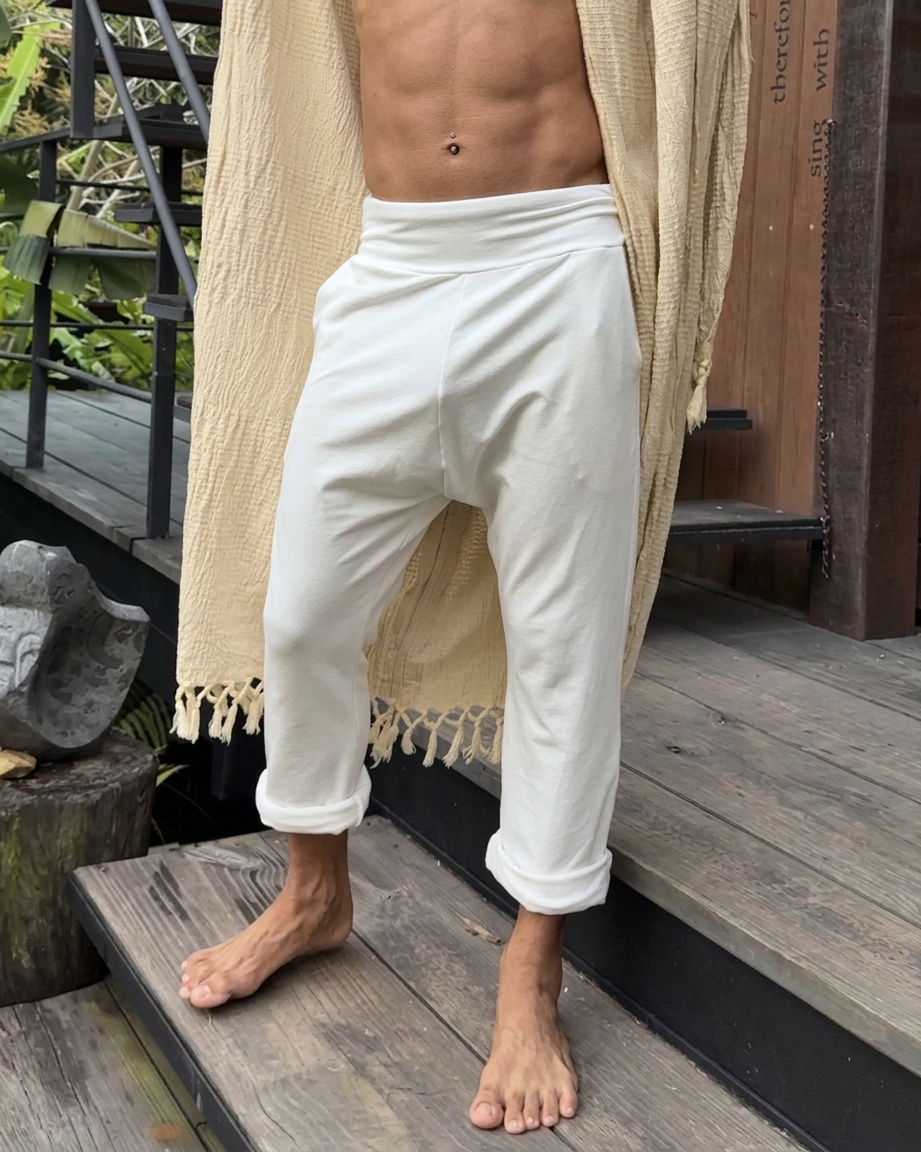 Person wearing white TOM pants by Glorka and a beige robe on a wooden deck.
