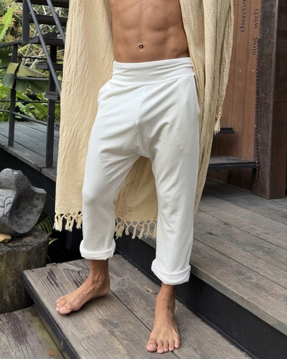 Person wearing white TOM pants by Glorka and a beige robe on a wooden deck.